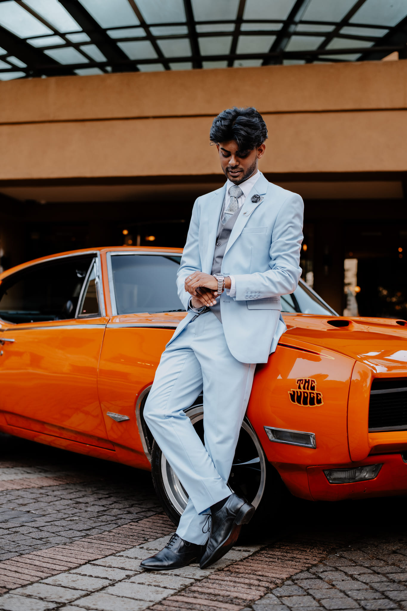  man in suit leaning on orange car 